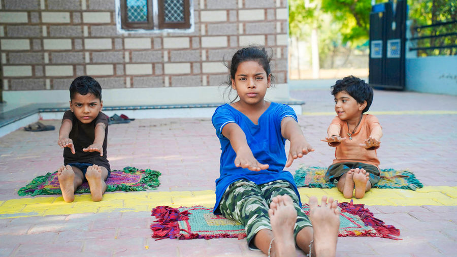 Three indian little kids doing meditate yoga asana on roll mat at home.