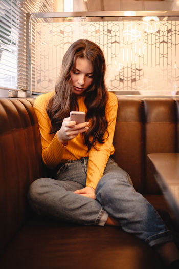 Teenage girl using smart phone while sitting in cafe