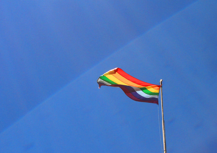 Low angle view of rainbow flag waving against blue sky