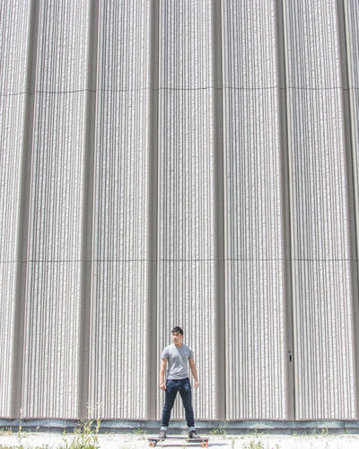 Full length of man standing on skateboard against wall