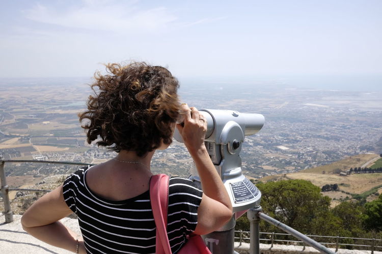 Rear view of woman looking through coin-operated binoculars from observation point at erice