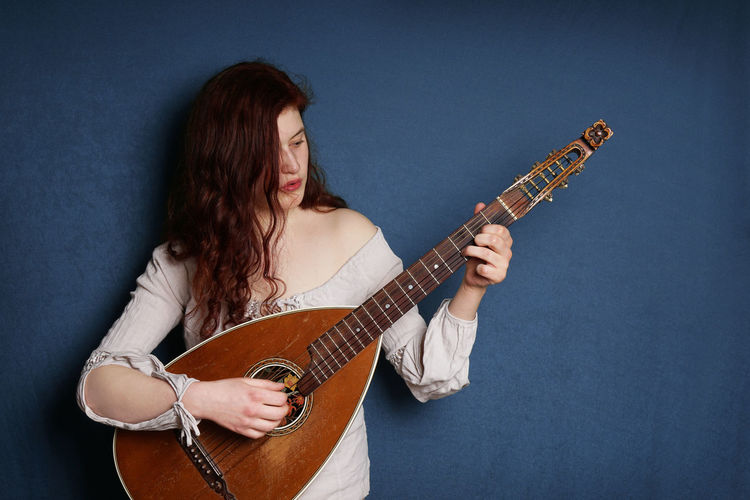 Young woman playing lute against blue wall