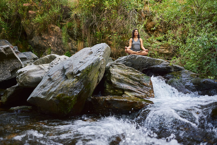 Young woman practicing yoga in a river. she's in the middle of nature.