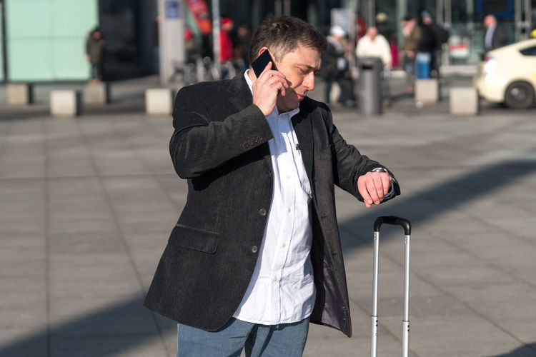 Man talking on mobile phone while checking time in city
