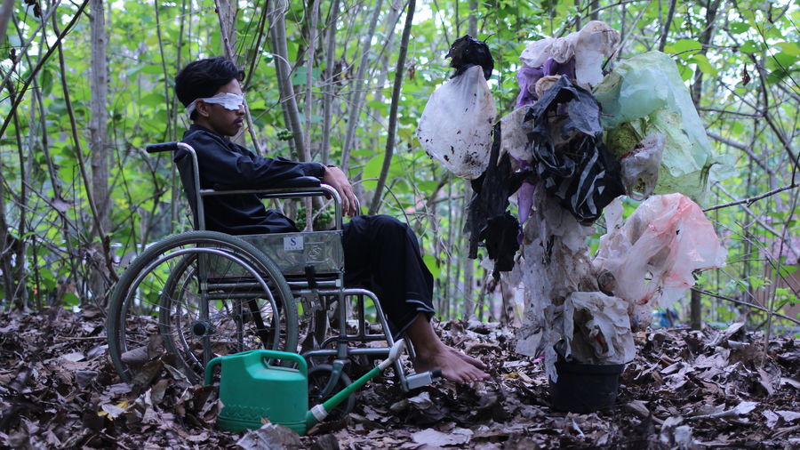 Man with blindfold sitting on wheelchair by plastic in forest