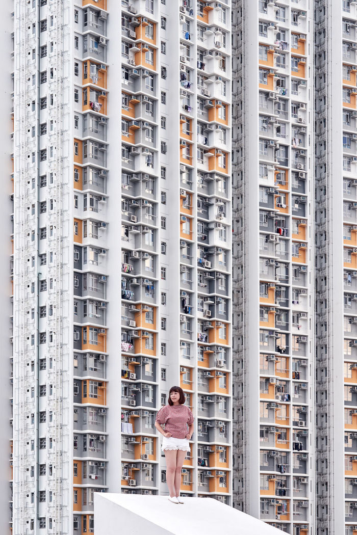 LOW ANGLE VIEW OF WOMAN STANDING AGAINST BUILDINGS