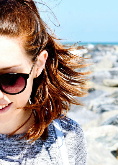 Close-up of woman wearing sunglasses against rocks and sky