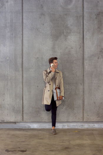 Young model using mobile phone while leaning on wall