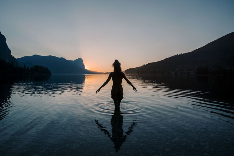 Austria, mondsee, lake mondsee, silhouette of woman standing in water at sunset