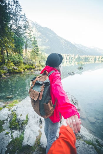 Woman holding cropped hand of friend while standing at lakeshore