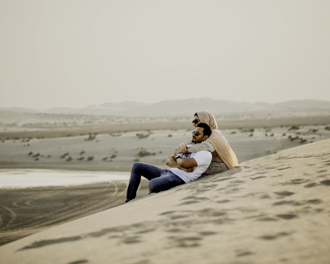 Couple sitting on sand in desert