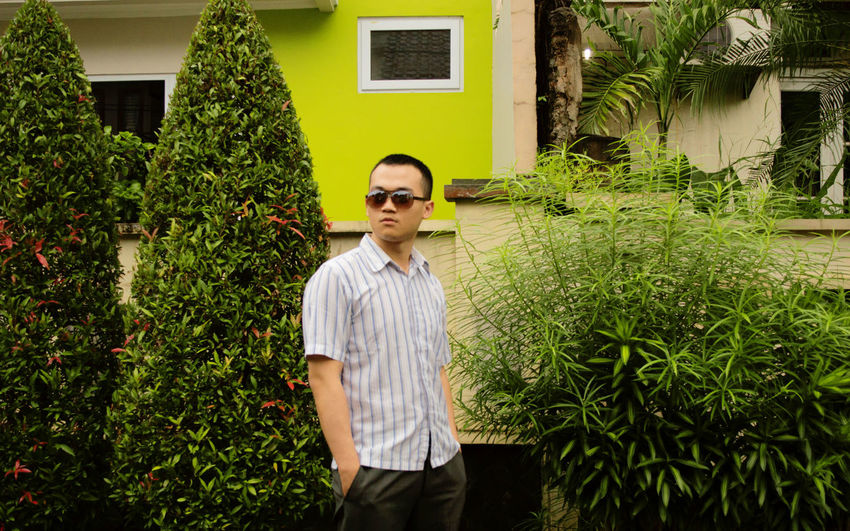 Young man wearing sunglasses standing by plants against building
