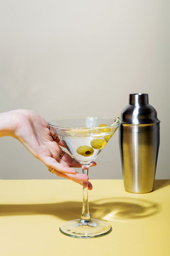 Female hand with rings holds glass of martini cocktail with olives. focus on shadows