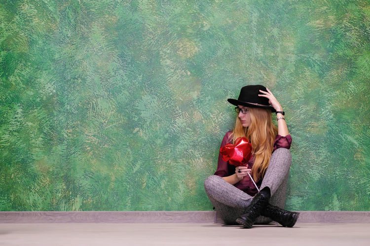 Young woman in hat sitting on wall