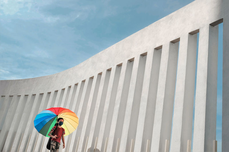 Low angle view of boy with multi colored umbrella against sky