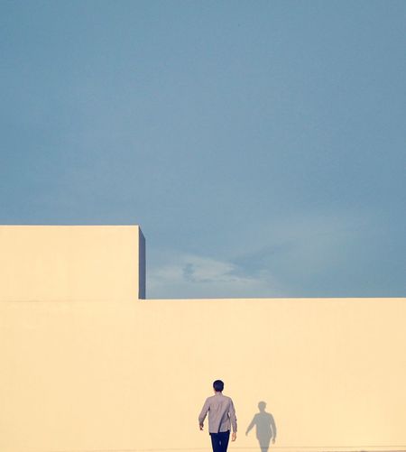 Rear view of man walking towards building against sky