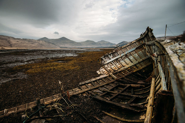 Damaged ship by river against cloudy sky