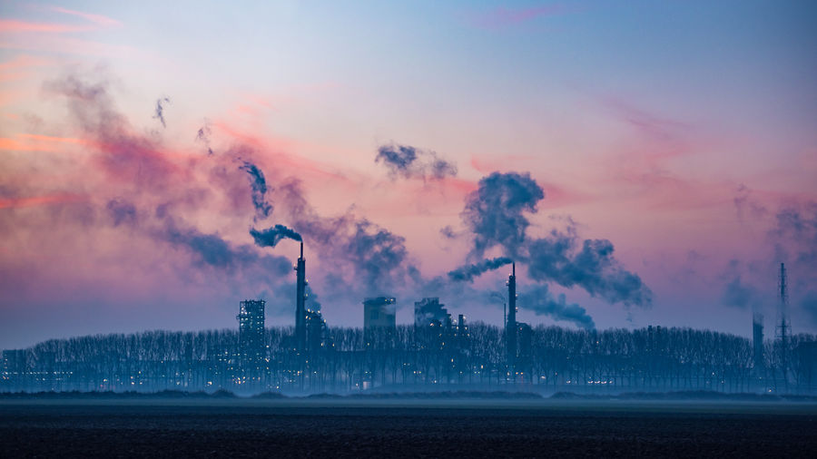 Smoke emitting from factory against sky during sunset