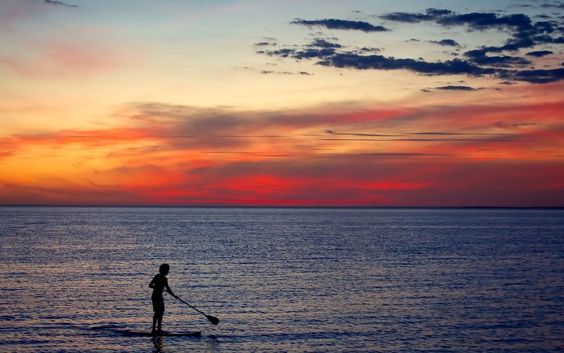 Silhouette man paddleboarding in sea against sky during sunset