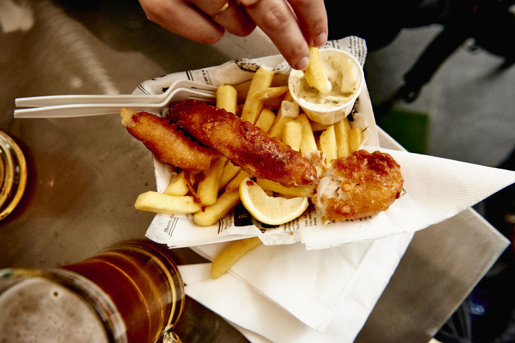 Cropped image of hand having french fries and sausage at restaurant