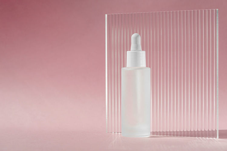 Serum oil in white transparent bottle with dropper on pink backdrop with acrylic ribbed sheet. 