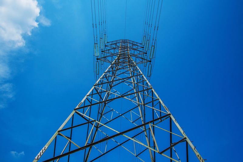 Low angle view of electricity pylon against blue sky