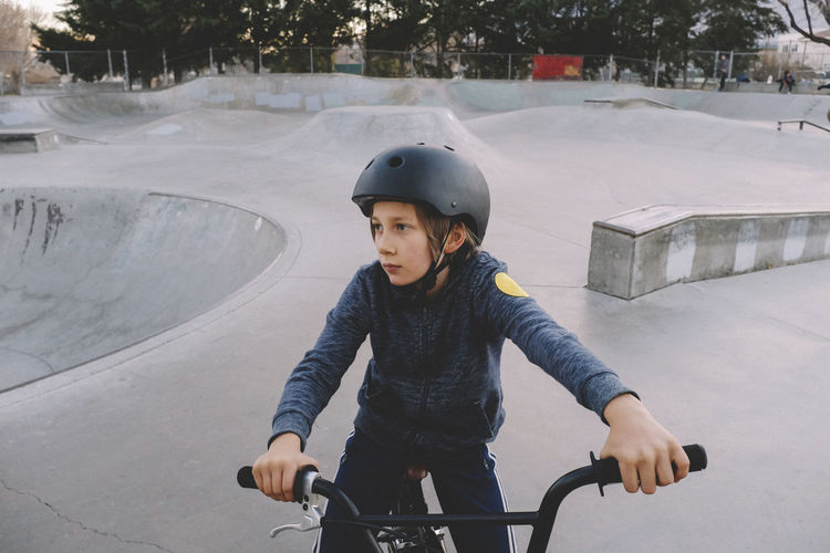 Boy wearing helmet while sitting on bicycle at skateboard park