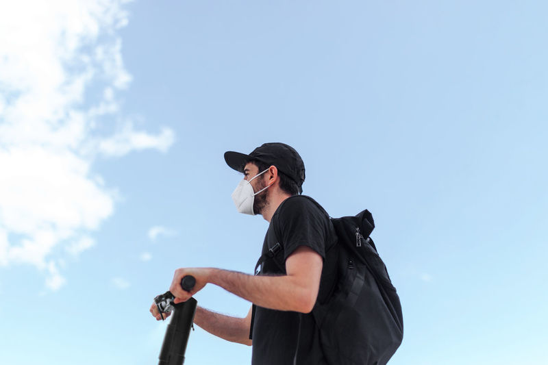 Man holding camera while standing against sky