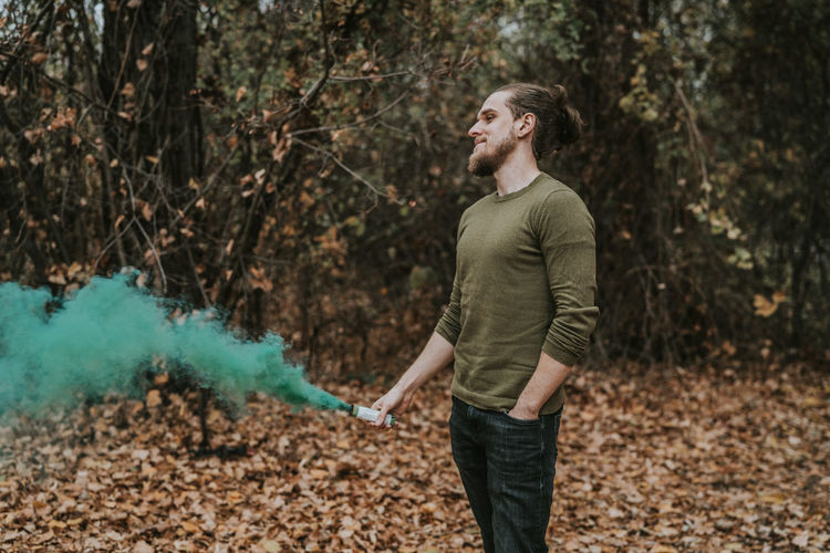 Young man holding distress flare while standing in forest during autumn