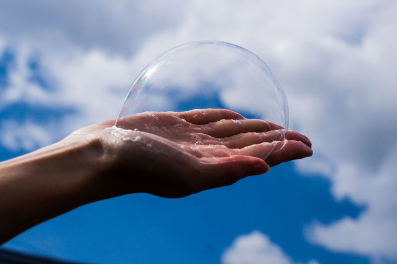 Close-up of hand holding bubbles against sky