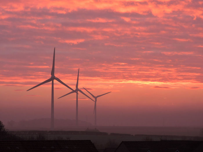 Silhouette of wind turbines against dramatic sky during sunset