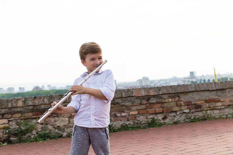 Boy playing flute against clear sky