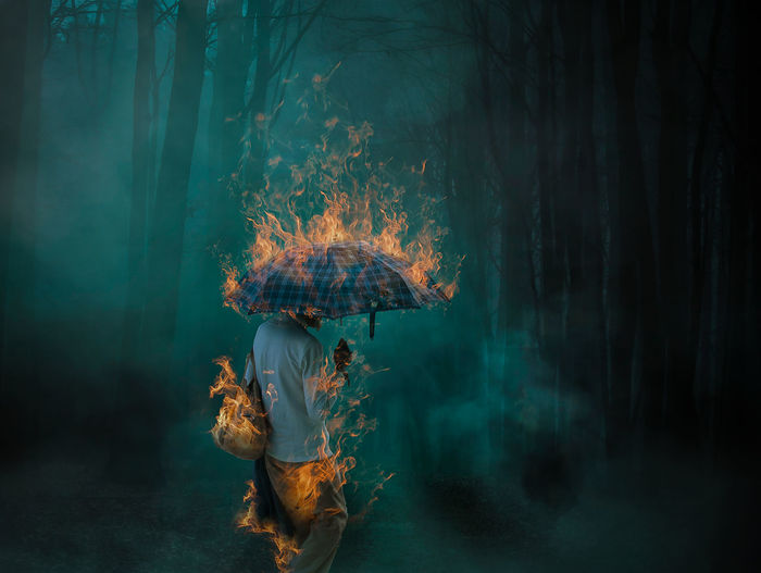 Digital composite image of woman standing with burning umbrella at night in forest