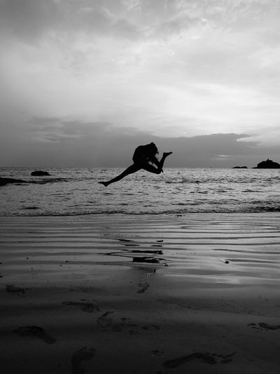 Silhouette person jumping on beach against sky