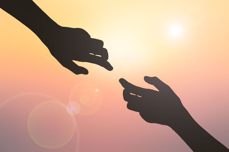 Cropped image of silhouette hands against shining sun during sunset