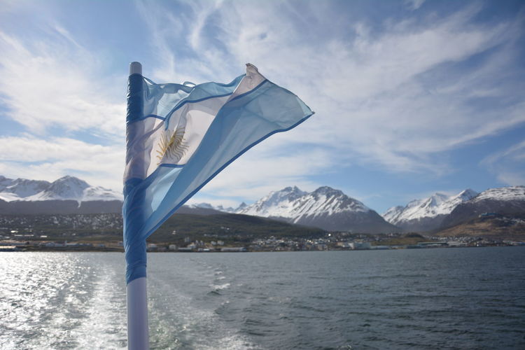 Argentinian flag by sea and snow covered mountains against sky