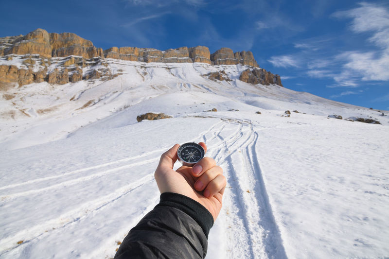 A man's hand holds a pocket magnetic compass for navigation against the backdrop of a rocky slope  
