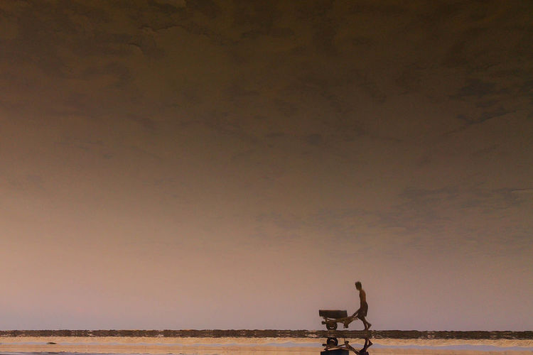 Manual worker pushing wheelbarrow against sky