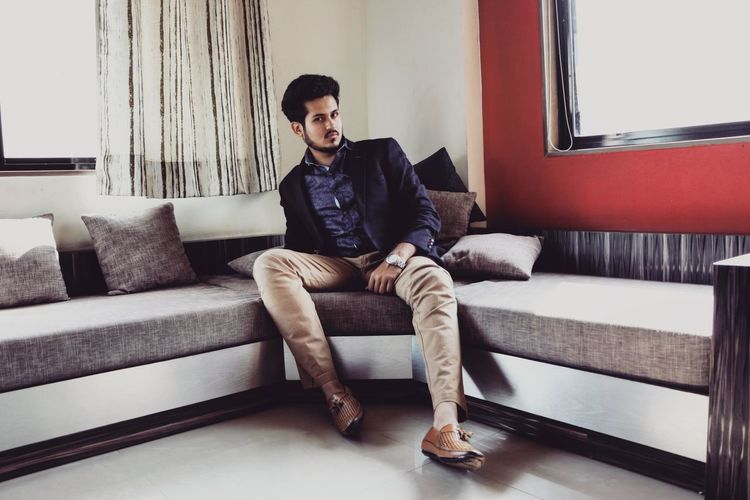 Full length portrait of young man sitting on sofa at home