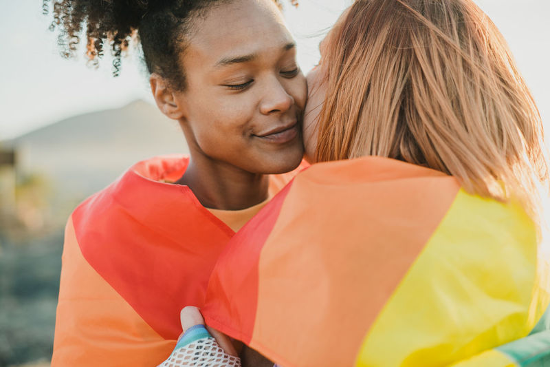 Loving multiethnic lesbian couple wrapped in flag hugging outdoors