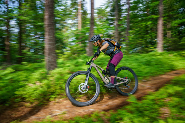 Woman riding mountain bike on footpath amidst trees in forest, austria