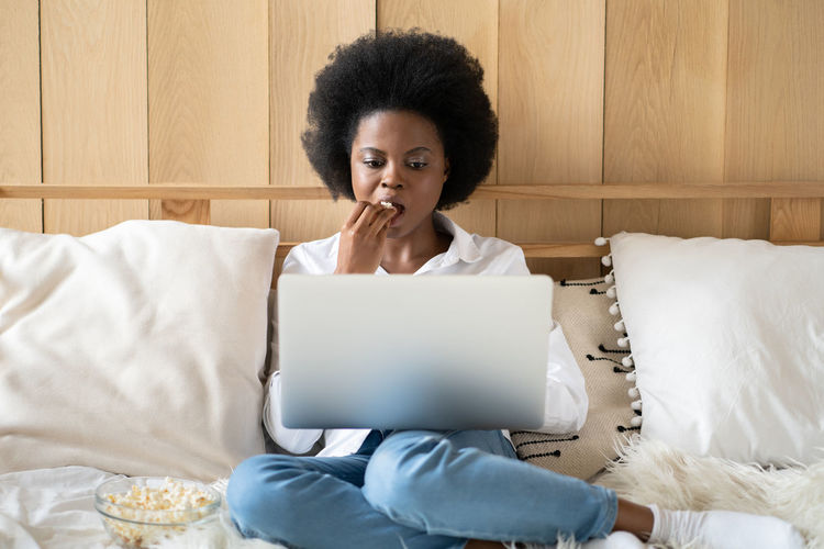 Young woman using laptop while sitting on bed