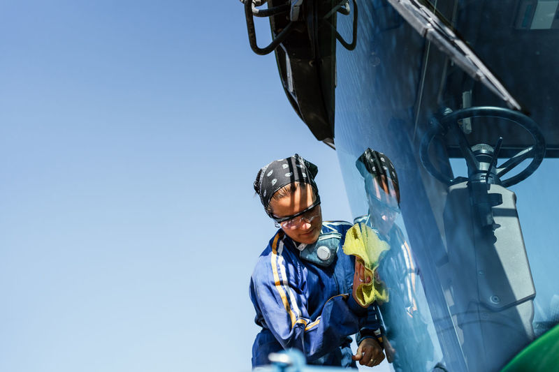 Side view low angle of busy female worker in uniform washing window of combine harvester parked in rural area