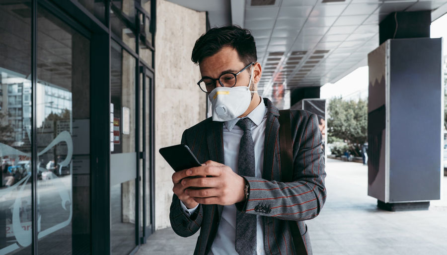 Business man with protective face mask using phone on city street.