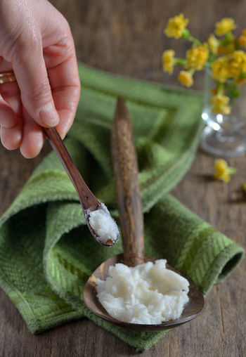 Close-up of hand holding wooden spoon with butter on table