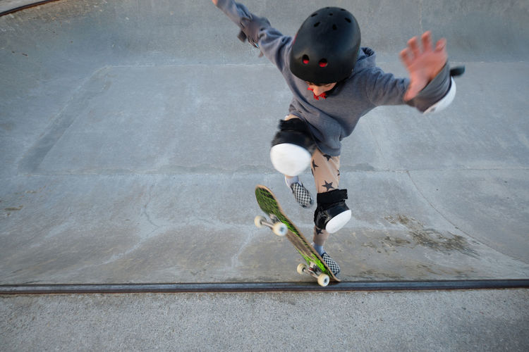 From above of teen boy showing stunt on skateboard while practicing on ramp and jumping in skate park