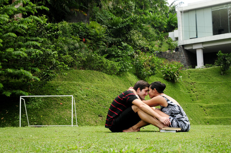 Side view of romantic couple embracing while sitting on grassy land