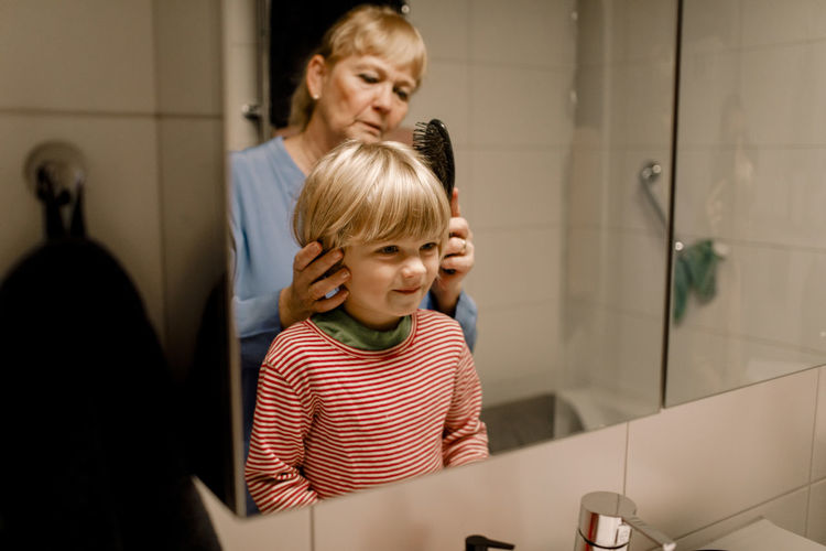 Senior woman combing hair of grandson in bathroom at home