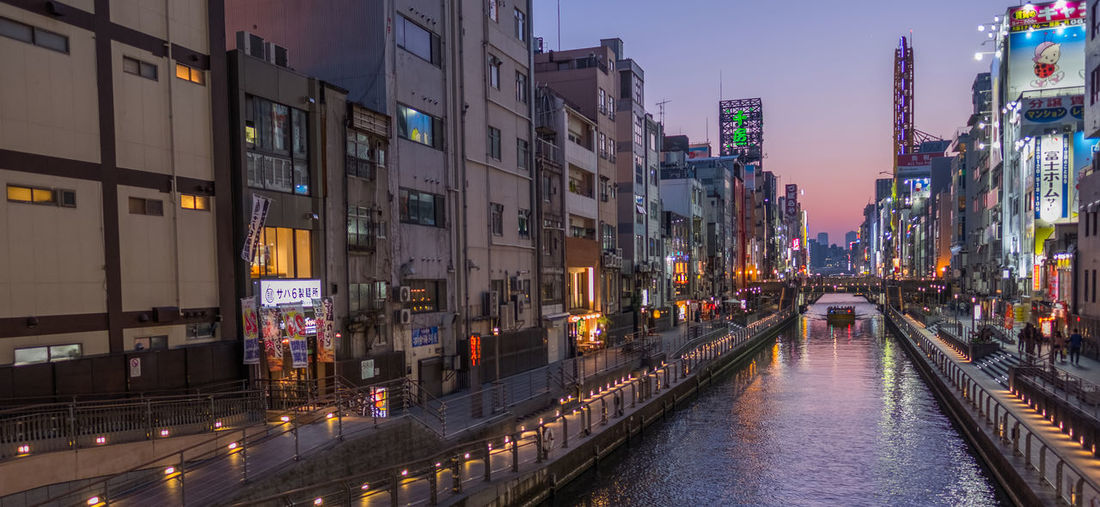 Canal amidst illuminated buildings in city during sunset