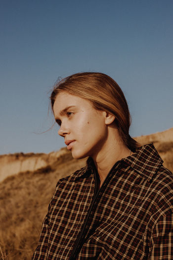 Portrait of young woman looking away against clear sky